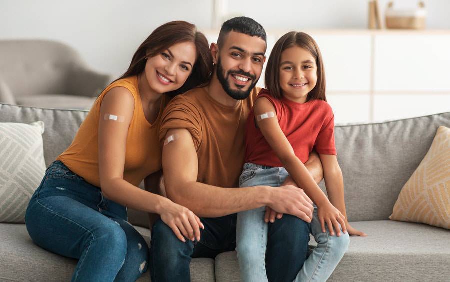 A young family shows off their arms with bandages after receiving either a shot, vaccine or immunization.