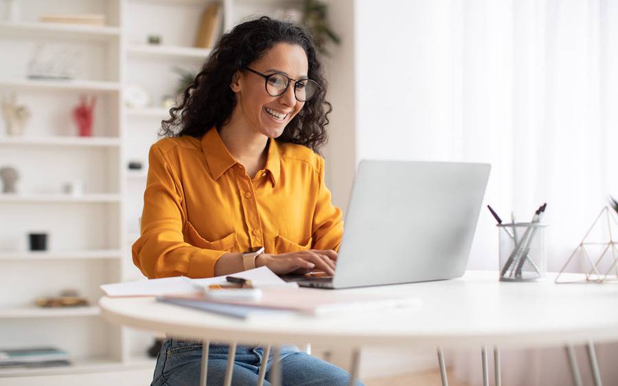 A young woman wearing eyeglasses smiles while looking at her laptop.