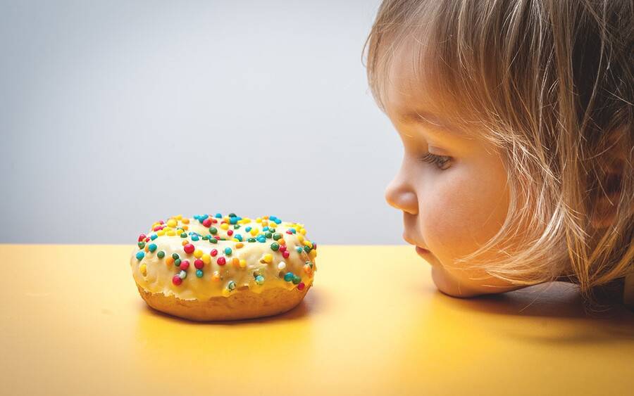 A young child stares at a colorful donut, with her chin on the tabletop.