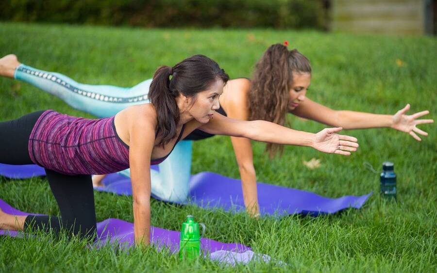 Two young women stretch in yoga poses on the grass outdoors.