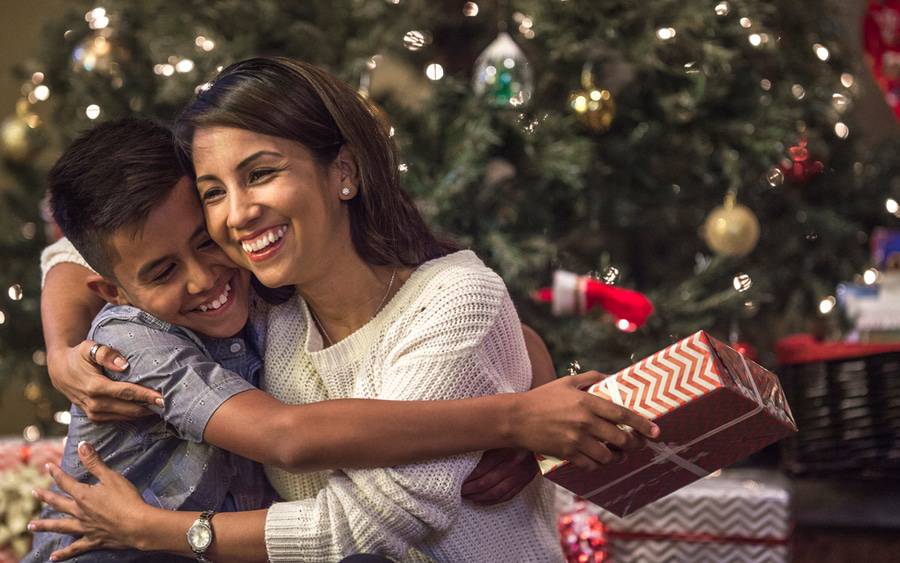A young mother hugs her son with a Christmas tree in the background.