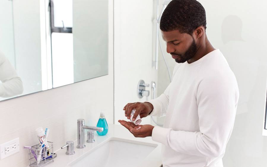 A man in his bathroom measuring out men's supplements in his hand.