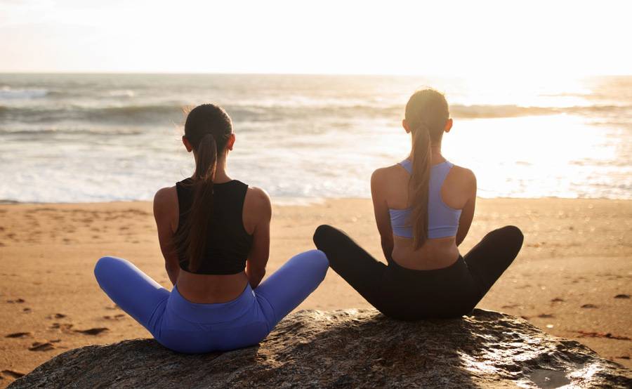 Two women sit with their legs crossed at the beach looking at the ocean helping to boost their immune system naturally.