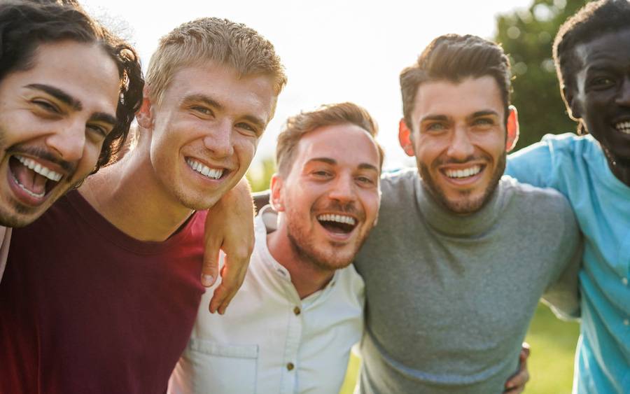 A group of diverse young men smile in an outdoors setting.