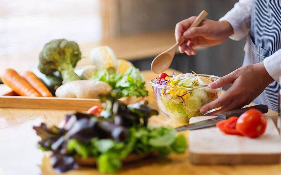 A healthy salad is being prepared with lettuce, purple cabbage, carrots, tomatoes and corn.