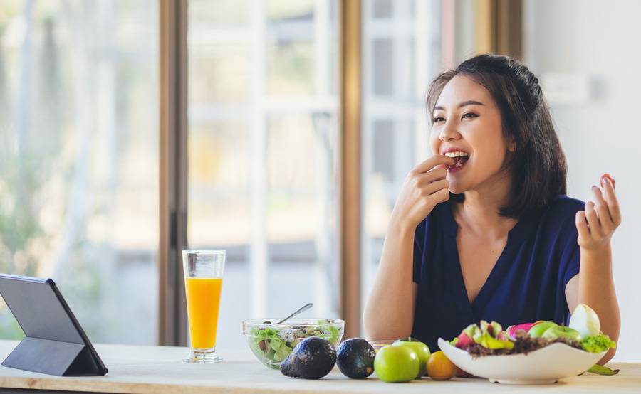 A young Asian woman eats a healthy meal with fresh fruit and veggies.
