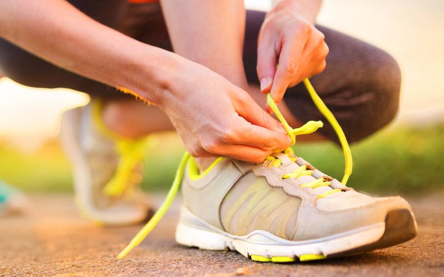 A woman's hands tie yellow shoelaces before a run. 