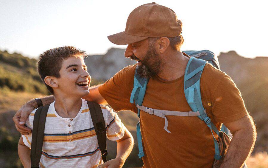A son and father looking at each other and having fun on their hike.