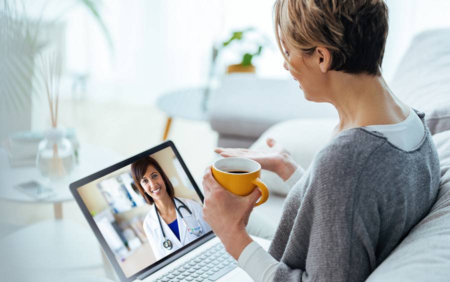 A woman sitting on her couch during her video visit with a provider as she has some tea.