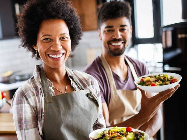 Two people holding bowls of food in a kitchen