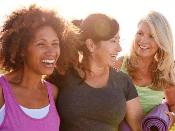 Three women of diverse backgrounds laugh together as they enjoy an afternoon outdoor yoga session.