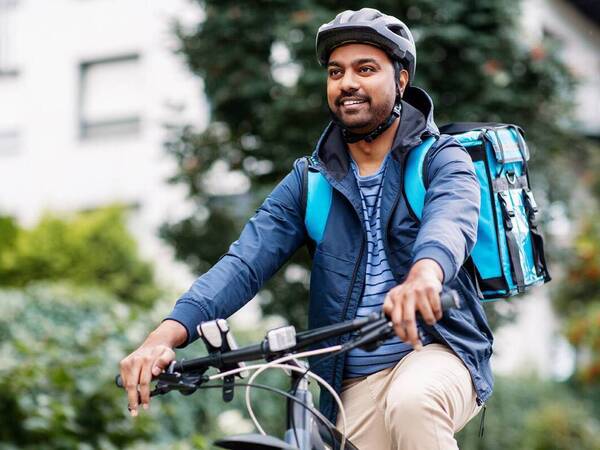 A young, black man bikes carrying a backpack and wearing appropriate helmet for safety.