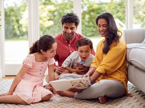 A young boy looks excited reading with his sister and parents around him.