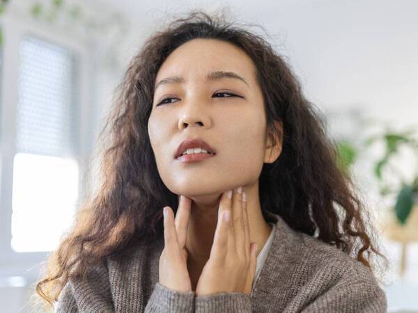 A young Asian woman touches her neck checking her thyroid glands.