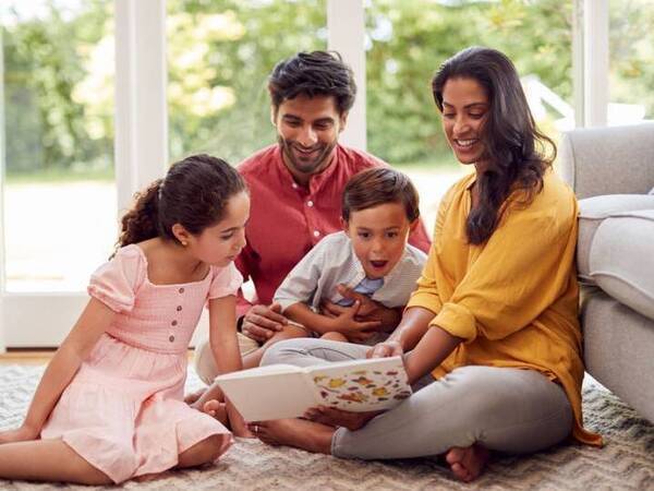 A young boy looks excited reading with his sister and parents around him.