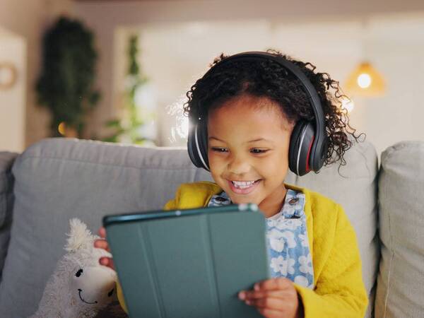 A child laughs while engaging with an educational online program on her tablet.
