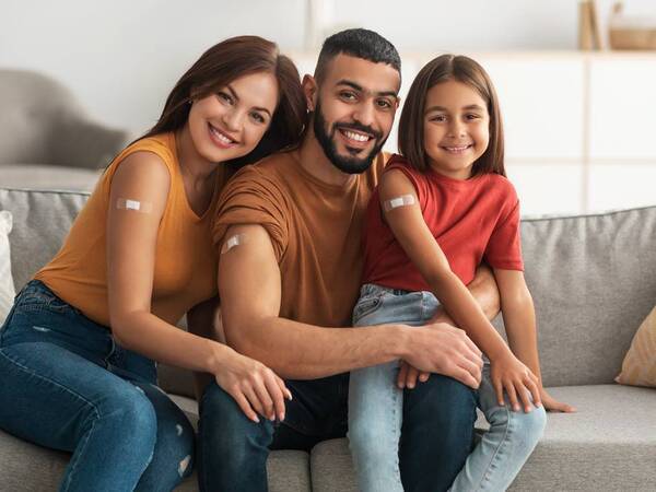 A young family shows off their arms with bandages after receiving either a shot, vaccine or immunization.
